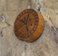 Load image into Gallery viewer, A round Holz Plug Teakholz Rune Leben Tod Punkte double flared, engraved with runic symbols and a prominent central rune, is displayed against a textured stone background.
