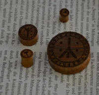Load image into Gallery viewer, Four round wooden pieces resembling the Holz Plug Teakholz Rune Leben Tod Punkte double flared are placed on an open book with German text. Their varied sizes evoke the look of an Ohr Piercing Plug set.
