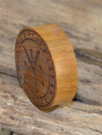Load image into Gallery viewer, A carved wooden token, inspired by the Holz Plug Teakholz Rune Leben Tod Punkte double flared, with rune-like symbols and decorative edge markings, rests on a rustic wooden surface.
