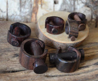 Load image into Gallery viewer, Several Plug Narraholz Pin-Creole braun gemasert Holz-Pin Creole napkin rings are displayed on a rustic wooden surface, with some resting on a round wooden slab in the background.
