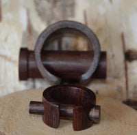 Load image into Gallery viewer, Two Plug Narraholz Pin-Creole braun gemasert Holz-Pin Creoles with unique geometric designs are displayed on a light wooden surface—one upright, one flat. The blurred wood texture background highlights their elegant appeal.
