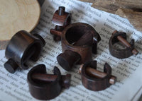 Load image into Gallery viewer, Several small, dark wooden puzzle pieces are arranged on an open book with German text. In the background, a Plug Narraholz Pin-Creole braun gemasert Holz-Pin Creole and some bark are visible.
