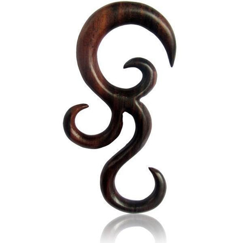 The Sonoholz lang hand-carved wooden spiral expander features an organic, abstract tribal-inspired design with flowing curves and pointed ends. Unisex ornament is presented on a white background with a subtle reflection below.