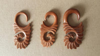 Load image into Gallery viewer, Three Piercing Holz red sawo wood Abstrakt S-Form Tribal earring Expander Dehner pieces, with spiral and leaf-like designs, are displayed side by side on a plain light brown surface.
