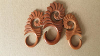 Load image into Gallery viewer, Three intricately carved Piercing Holz red sawo wood Abstrakt S-Form Tribal earring Expander Dehner with spiral and leaf patterns are arranged on a plain beige surface.
