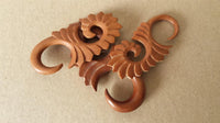 Load image into Gallery viewer, Two Piercing Holz red sawo wood Abstrakt S-Form Tribal earring Expanders, featuring intricate spiral carvings and pointed ends, are displayed on a plain brown surface, perfect as handgeschnitzter Ohrschmuck for lobe piercings.
