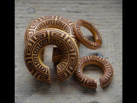 Load image into Gallery viewer, Four Ohr Donut Piercing griechisch Jackfrucht Holz Expander in various sizes, each with a small cut-out and geometric Greek key patterns burned into the wood, are arranged on a textured wooden surface.
