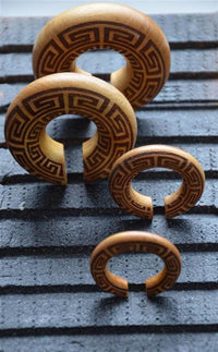Load image into Gallery viewer, Four crescent-shaped Ohr Donut Piercing griechisch Jackfrucht Holz, featuring geometric patterns, are displayed on a textured black surface in size order from largest at the back to smallest at the front.
