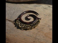 Load image into Gallery viewer, The Piercing Dehnschnecke Narraholz Brass Ornament Spirale features a spiral design in Narra wood with detailed brass accents, shown on a textured wooden surface—ideal for fans of unique lobe piercings.
