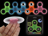 Cargar imagen en el visor de la galería, A hand spins a pink Turbo Fidget Spinner Tri (dreifach) leuchtend Glow in the dark Spielzeug Kreisel, with motion blur, above five colorful Kreisel and a black box.
