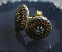 Load image into Gallery viewer, A close-up of Messing Stein Ohrstecker antik gold Dahlie 10mm featuring intricate lattice patterns and central blue stones, these vintage-style earrings evoke classic elegance, displayed on a dark reflective surface.
