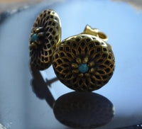 Load image into Gallery viewer, A pair of Messing Stein Ohrstecker antik gold Dahlie 10mm with intricate floral cut-out design and small turquoise centers, displayed on a reflective dark surface.
