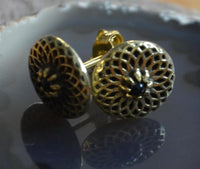 Load image into Gallery viewer, A close-up of Messing Stein Ohrstecker antik gold Dahlie 10mm, featuring an intricate circular filigree inspired by the dahlia flower and a dark central stone, displayed on a reflective surface.
