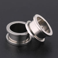 Load image into Gallery viewer, Two silvery Metalltunnel Tunnel Chirurgenstahl Unisex Edelstahl Plug Expander Piercings with smooth, reflective finishes rest on a dark surface—one standing upright, the other leaning against it, each featuring flared edges.
