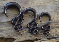 Load image into Gallery viewer, Three dark brown, twisted Holz Lobe Piercing Dehner displayed on rustic wood—unique ear gauges for your lobes.
