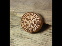 Load image into Gallery viewer, A Flesh Plug Teakholz Vegvisir Runen Ring, double flared and engraved with Norse runes and a Vegvisir compass, lies on a textured wooden surface.
