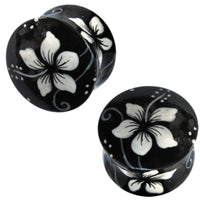 Load image into Gallery viewer, Two black round Holz Plug Hawaii Blume aus Teakholz, handbemalt mit weißen Blüten und filigranen Details, werden in verschiedenen Winkeln auf weißem Hintergrund gezeigt – stilvoller, handgefertigter Schmuck.
