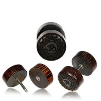 Load image into Gallery viewer, Four round, dark wooden fake plugs with engraved Om (ॐ) symbols are displayed on a white background. Three lay flat to show the design, while one Fake Motiv Holz Plug Piercing Edelstahl mit Om is stacked upright for a unique look.
