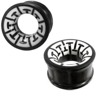 Load image into Gallery viewer, Two black "Tribal Holz Tunnel" ear plugs, hand-carved from ironwood with white bone inlays featuring a geometric black pattern. These cylindrical plugs blend modern style with traditional design.
