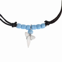 Load image into Gallery viewer, A Surferkette Haifzahn necklace with a black cord, five light blue beads, and a wire-wrapped Haifischzahn pendant. Features round wooden and shell accents and an adjustable length.
