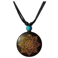 Load image into Gallery viewer, The Halskette Holz Türkis verstellbar Anhänger gold silber features a round, dark wood pendant with a gold mandala design on an adjustable cotton cord, finished with a single turquoise bead above the pendant.
