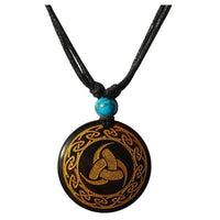Load image into Gallery viewer, The Halskette Holz Türkis verstellbar Anhänger gold silber features a round black pendant with gold Celtic knot and border, plus a turquoise bead, all hanging on an adjustable cotton cord for a versatile unisex look.

