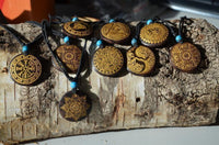 Load image into Gallery viewer, The Halskette Holz Türkis verstellbar Anhänger gold silber features unique geometric or symbolic designs with gold patterns and blue beads on a verstellbare Baumwollkette—perfect as a unisex necklace.
