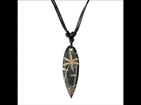Load image into Gallery viewer, The Surferkette Holz Halskette Gravur, a black wood surfboard-shaped necklace with tan-engraved palm tree, birds, and waves, hangs from an adjustable black cotton cord against a white background.
