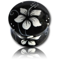 Load image into Gallery viewer, A round, glossy black Holz Plug in Teakholz, handbemalt with a white Hawaii Blume design inspired by Hibiskus motifs. The large petals and delicate swirls create a soft reflection beneath the stylish body jewelry.
