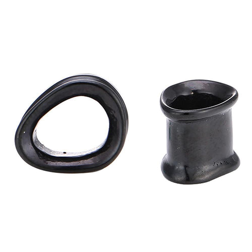 Two glossy black “Schraubplug Tunnel Triangle” plugs made of surgical steel are shown on a white background; one is concave and triangular, while the other is cylindrical with a wide base and uneven top edge.