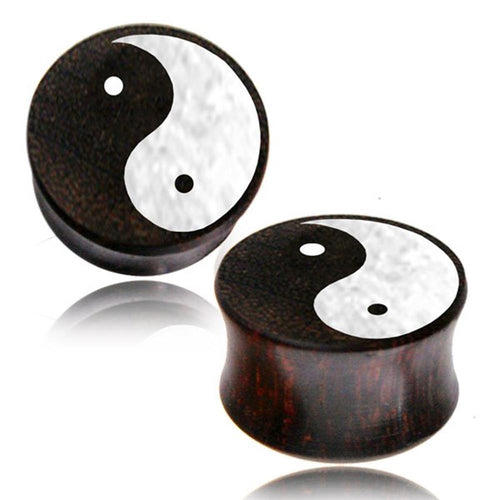 Two cylindrical black Holz Plug Tamarinde Yin Yang Bone Powder Inlay Tunnels feature a striking Yin Yang symbol on the front, representing balance. Inspired by Tribal Expander designs, these stylish gauges are shown on a white background.