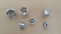 Load image into Gallery viewer, Seven metallic ear gauges, including the Edelstahl Tunnel Plug Flügel Herz Stein facettiert Schraubplug double flared, are displayed on a light wooden surface; some feature charms, and one has a heart-shaped design.

