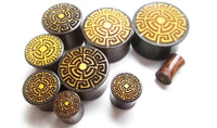 Load image into Gallery viewer, Nine round Plug Tamarindenholz griechisch Sonne Ornament Spiralen Inlay double flared flach plugs in assorted sizes, each with a gold sun spiral inlay, are displayed on a white background.
