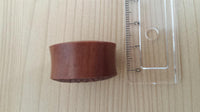 Cargar imagen en el visor de la galería, A Plug Sawo Holz braun Gravur schwarz Blüte Herz Tribal Expander Organic Tunnel sits beside a clear ruler on light wood; the ruler shows the plug is about 2 centimeters tall.
