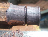 Load image into Gallery viewer, A close-up of the Sawo Holz Plug Gravur handgeschnitzt Gesicht Sonne being turned on a lathe, showing its partially shaped profile with a distinct groove, smooth surfaces, and surrounded by wood shavings.
