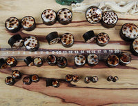 Load image into Gallery viewer, Organic Arangholz Plug Black Dots Shell Inlay weiß dunkel Tribal earrings are arranged by size on a wooden surface beside a clear centimeter-marked plastic ruler.

