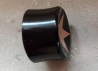Load image into Gallery viewer, A Horn Plug Stern Inlay metallic rosegold schwarz Expander Flesh Tunnel, handmade, with a metallic rosegold star on top, is shown on a light gray, slightly textured background.
