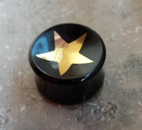 Load image into Gallery viewer, A Horn Plug Stern Inlay metallic gold schwarz Expander Handarbeit Flesh Tunnel sits on a speckled gray surface.
