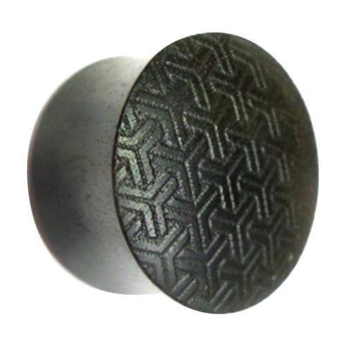 A round, dark, metallic Flesh Plug Ebenholz Peace Knoten Muster features a flat face with an intricate, interlocking Y-shaped pattern engraved on its surface and a slightly reflective finish.