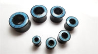 Load image into Gallery viewer, Seven black cylindrical plugs featuring blue-patterned tops, including the Flesh Tunnel Eisenholz schwarz Rim Crushed Türkis Inlay, are arranged on a white surface in descending size order, forming a gentle arc.
