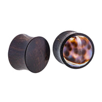 Load image into Gallery viewer, A pair of Organic Arangholz plugs, one smooth and one featuring a glossy white and dark shell inlay with black dots in a tribal design.
