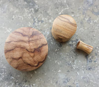 Load image into Gallery viewer, Three hand-carved wooden tampers of varying sizes rest on a gray, speckled surface. Each features a rounded top and smooth, polished wood grain similar to the Olivenholz Flesh Plug Lobe Piercing Holz Double Flared.
