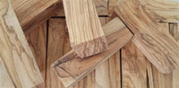 Load image into Gallery viewer, Several rectangular blocks of Olivenholz Flesh Plug Lobe Piercing Holz Double Flared, each showing unique dark grain patterns, are stacked and scattered on a matching hand-carved wooden surface.
