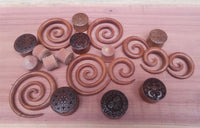 Load image into Gallery viewer, A set of brown Sawoholz Holz Flesh Plugs with "Gesicht Krieger" engravings, displayed on wood. The plugs vary in size and showcase detailed tribal and Aztec-style designs.
