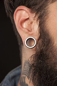 Load image into Gallery viewer, A close-up of a person’s ear wearing the Holz Flesh Tunnel Perlmutt Inlay weiß Plug in dunkelbraun. The individual has a beard, short dark hair, and a visible neck tattoo.
