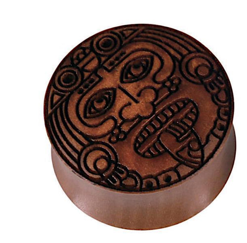 A round, brown Sawoholz Holz Flesh Plug named "Gravur Gesicht Krieger," featuring engraved stylized eyes, geometric patterns, and symmetrical shapes, viewed from above on a white background.