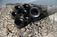 Load image into Gallery viewer, A selection of Eisenholz Tunnel schwarz fein gemasert Holztunnel handgeschnitzt Tribal Holz Plug Expanders in different sizes is displayed on textured wood, with light accentuating the tunnels' fine grain and the wood's natural details.
