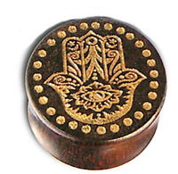 Load image into Gallery viewer, A round Holz Plug named "Poor Mans Hand" is crafted from Tamarind wood, laser-engraved with a gold-painted Khamsa (Fatima hand) design featuring an eye and surrounded by a ring of gold dots in a tribal style.
