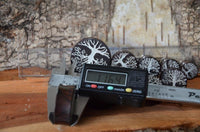 Load image into Gallery viewer, A digital caliper measures a round, dark Holz Plug Baum des Lebens Yggdrasil silber double flared with a white tree design, showing 11.64 mm. Transparent rulers and similar patterned plugs lie on the wood surface nearby.
