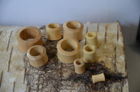 Load image into Gallery viewer, Several smooth, cylindrical Holz Flesh Tunnel Krokodilholz hell leicht konvex double flared rings in various sizes are arranged on birch bark, highlighting their natural light wood color and rustic handmade craftsmanship.
